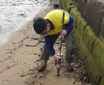 Bowen conducting soil sampling using hand auger on sandy shoreline