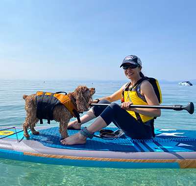 Carola sitting on a paddle board with her dog in the water.