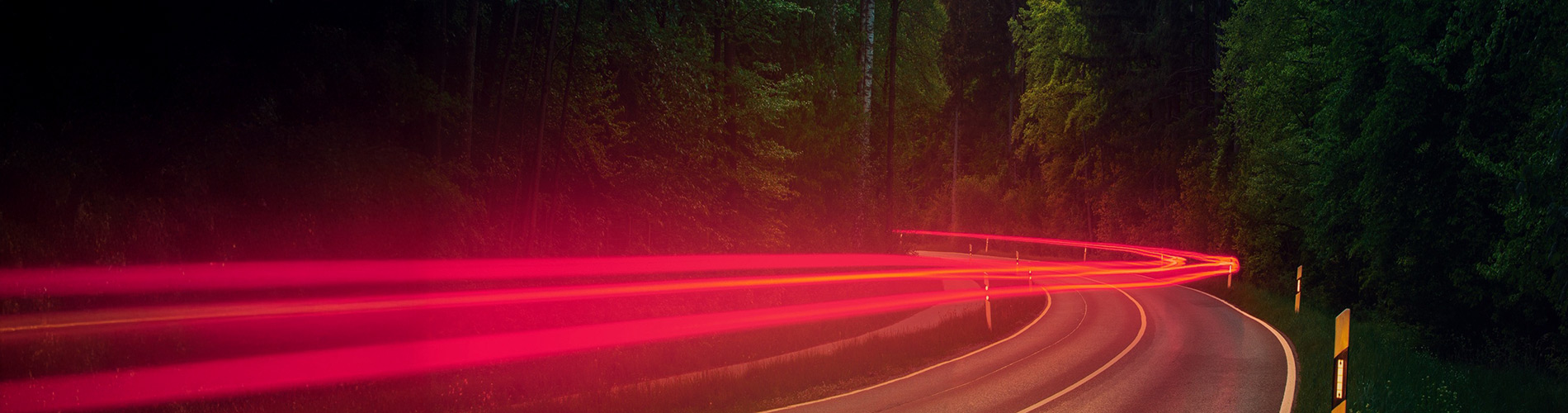 Vehicle red tail lights along a winding road through a forest.