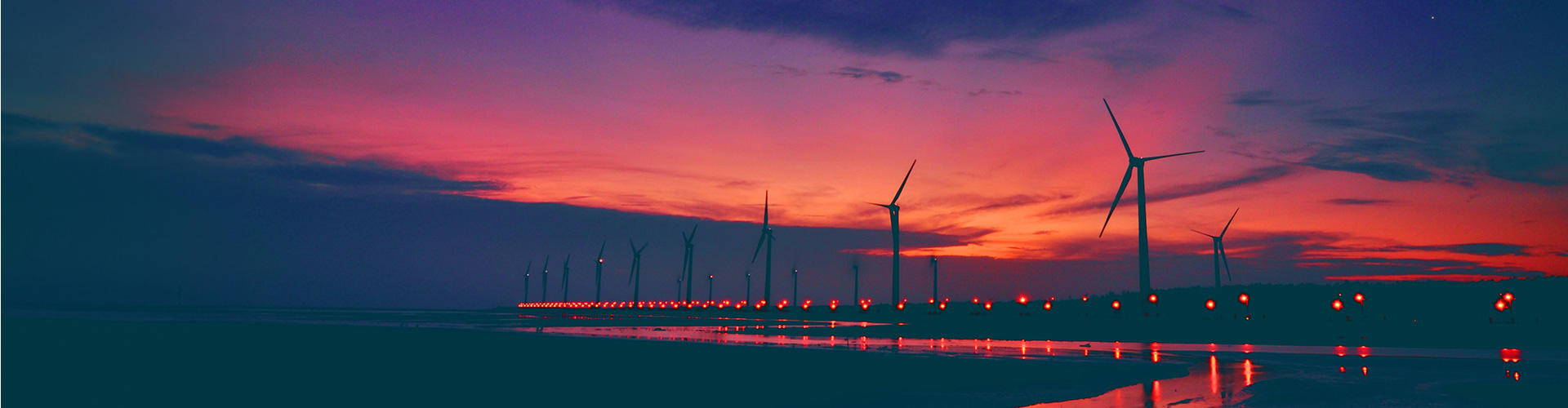 Rows of wind turbines against a dark orange sky.