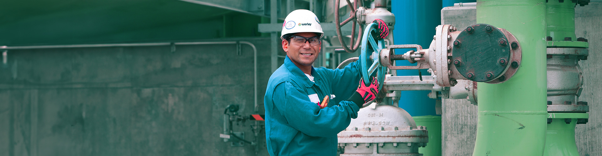 Worker wearing safety helmet turning a wheel on a large piece of machinery.