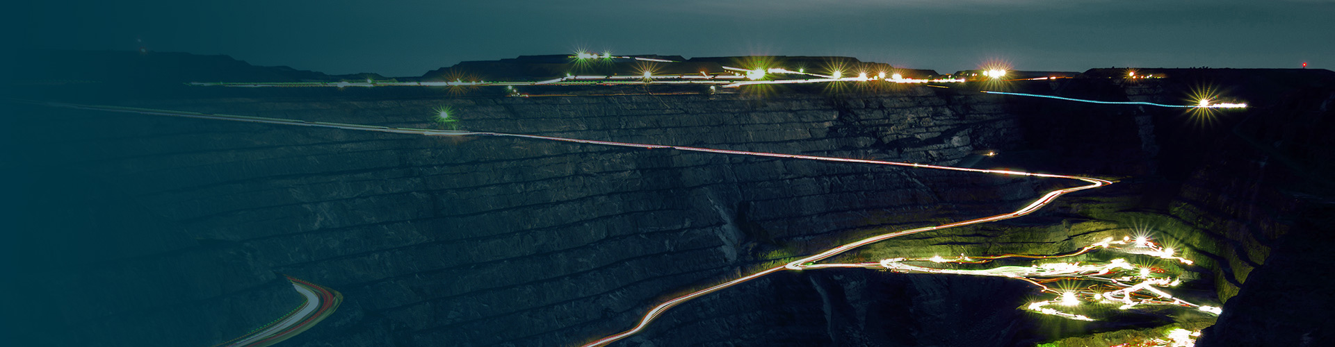 Night view of an open-pit mine with winding roads illuminating by vehicle lights.