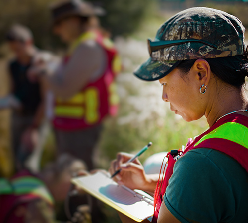 Three people working outside in the grass writing notes on paper.