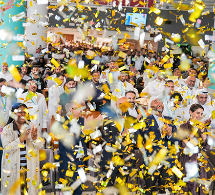Large group of  people from the Saudi Arabia office cheering with gold streamers falling down.
