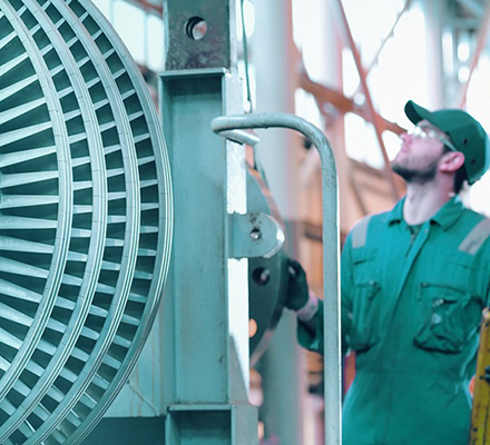 Engineer inspecting large industrial turbine machinery inside a power or processing facility.