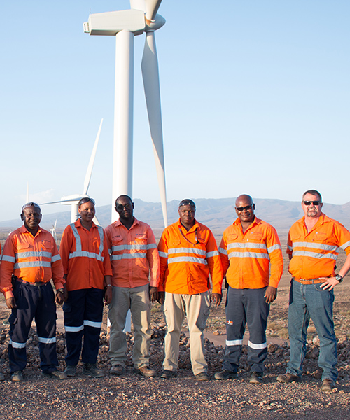 Group of Worley people standing in front of wind turbines at the Lake Turkana Wind Farm.