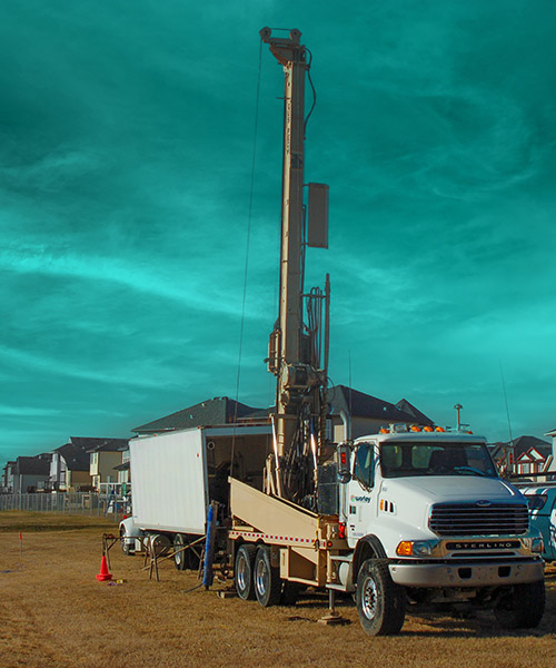 Truck with machinery parked next to a road and houses.