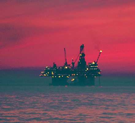 Offshore oil rig in the ocean with a red sky.