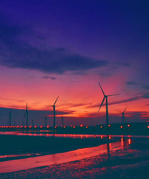 Rows of wind turbines against a dark orange sky.