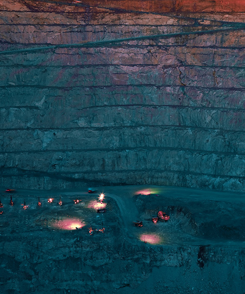Looking into an open mine with several mining vehicles with lights on.