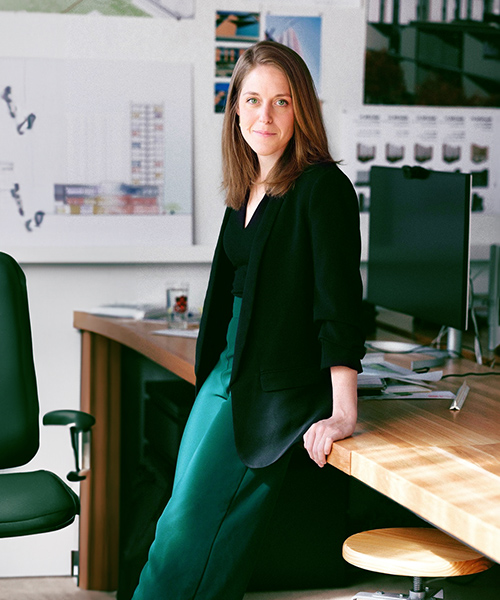 Woman leaning against an desk in the office.