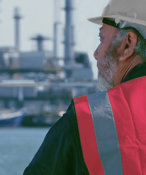 Man wearing PPE looking out onto an oil refinery.