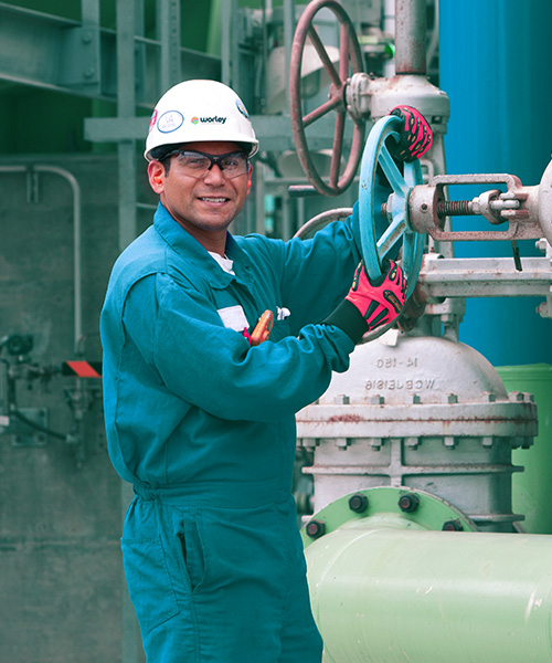 Worker wearing safety helmet turning a wheel on a large piece of machinery.