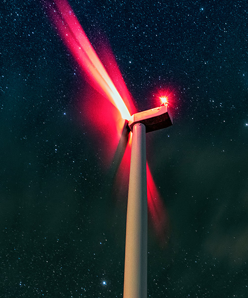 Looking up at the top of a wind turbine illuminated with bright colorful lights.