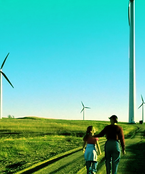 Adult and child walking together down a road through wind turbines.