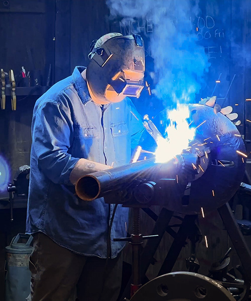 Person wearing safety equipment welding metal in a factory.
