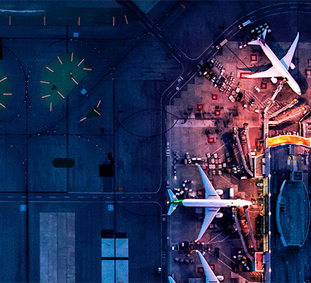 Aerial night view of an airport terminal with aircraft at gates and illuminated runways.