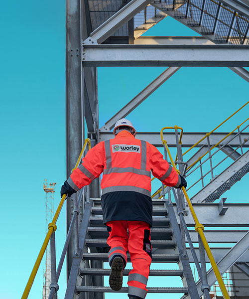 Person wearing PPE walking up stairs in a steel structure.