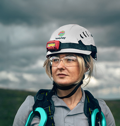 Woman wearing a Worley safety helmet with wind turbines in background.