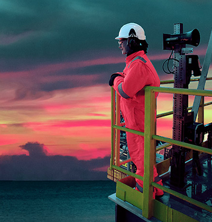 Person in PPE standing by the rail of an offshore oil platform looking out to sea.