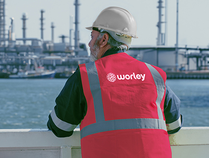 Man wearing PPE looking out onto an oil refinery.