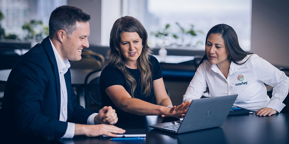 Three Worley people looking at a laptop screen together.