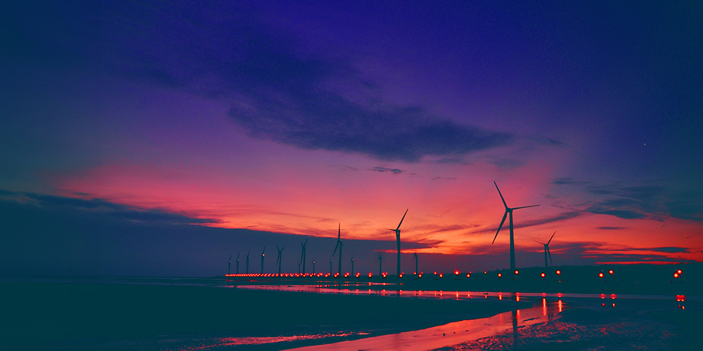 Rows of wind turbines against a dark orange sky.
