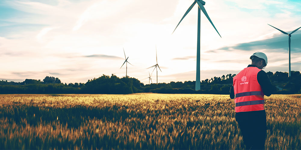 Person wearing Worley PPE next to a wind farm.