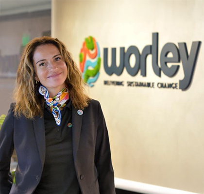 Andrea standing in front of Worley logo on the office wall.