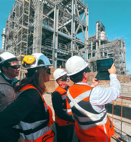 Andrea with 3 colleagues looking at a tablet in front of a large steel structure.