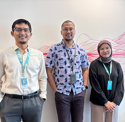 Febry standing in the middle of two colleagues in the office.
