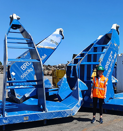 Hannah wearing safety gear standing in front of large blue steel lifting structures.