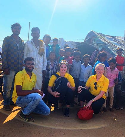 Harriet kneeling with two colleagues from the Pollinate Fellowship in front of a group of adults and children in India.