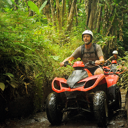 Tony on a red quad bike traveling along a muddy forest trail.