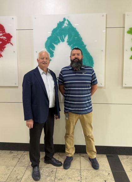 Will standing next to a colleague inside the office in front of Worley's Values prints on the wall.