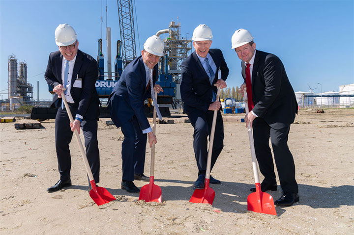 Four men wearing suits and hard hat digging the dirt with shovels.