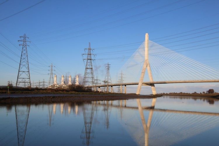 A scenic view of a bridge over a river, with tall trees nearby and power lines