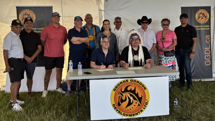 Twelve members of the Wicehtowak Worley JV, two members sitting at a table signing document.