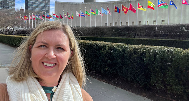 Gillian standing in front of the UN General Assembly Building with row of flags.