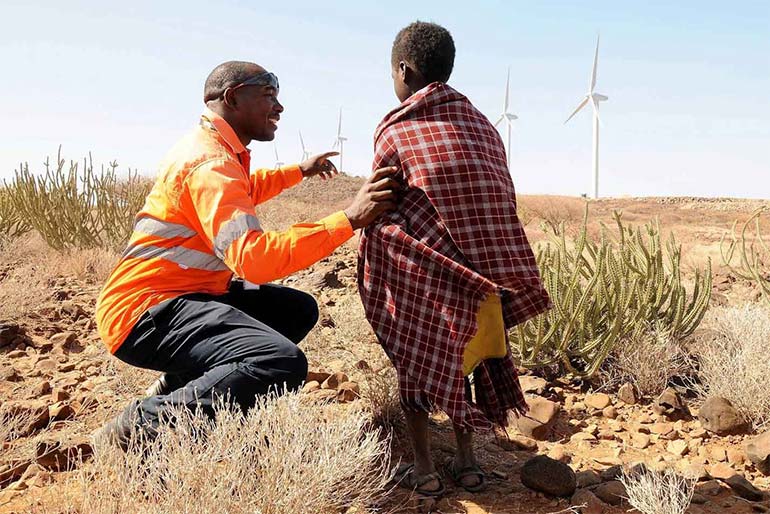 Man wearing fluroescent work clothes next to a child pointing to wind turbines.