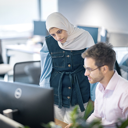 Worley woman standing next to a man seated at a computer.