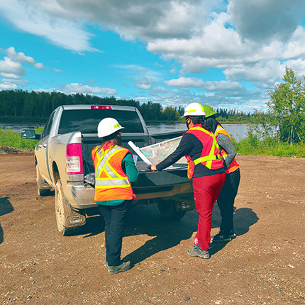 Three people wearing PPE standing at the back of an open ute looking at a map.