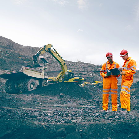 Two workers on a mine site next to a mine machinery.