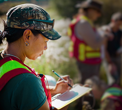 Group of people outdoors with a woman writing on a clipboard.